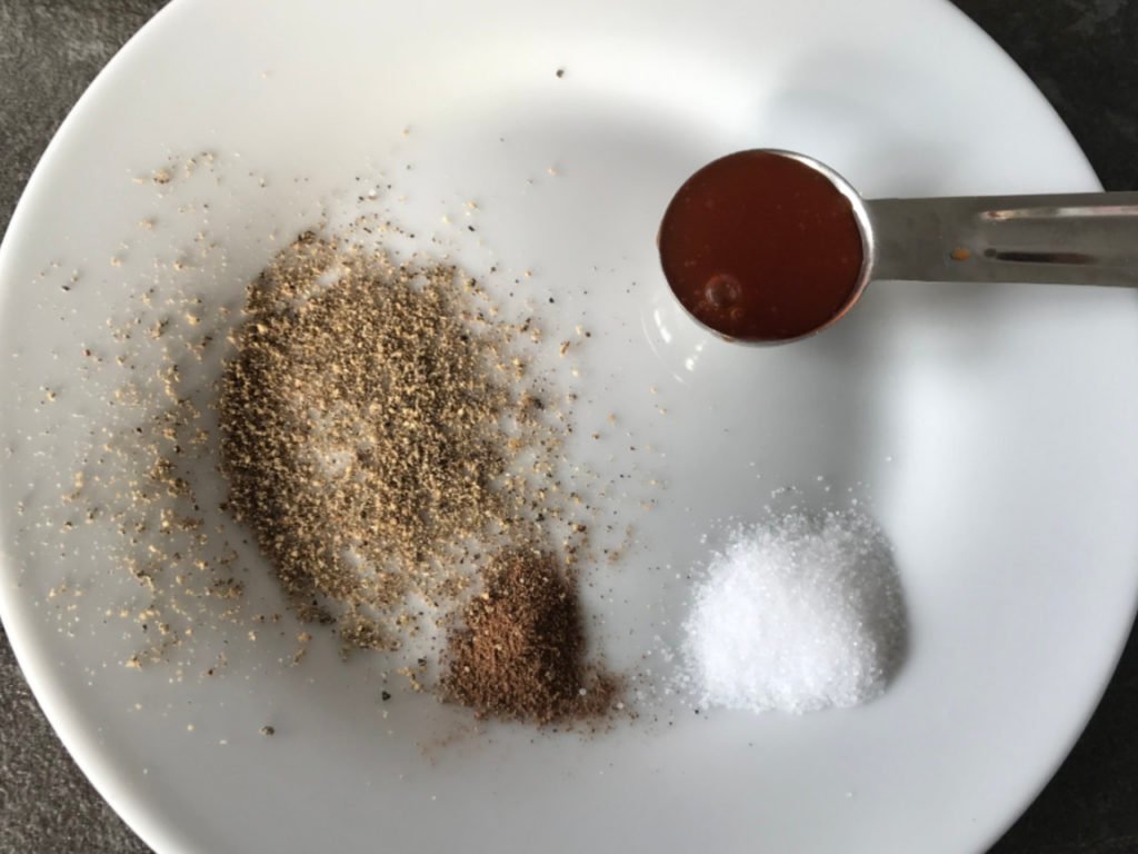 Salt, pepper, allspice, and Tabasco sauce measured out on a plate.