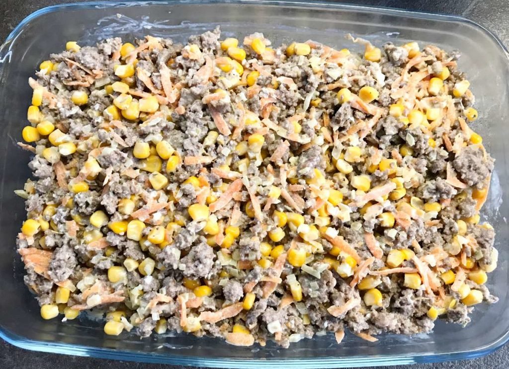 Ground beef and veggies layered with rice in a casserole dish.