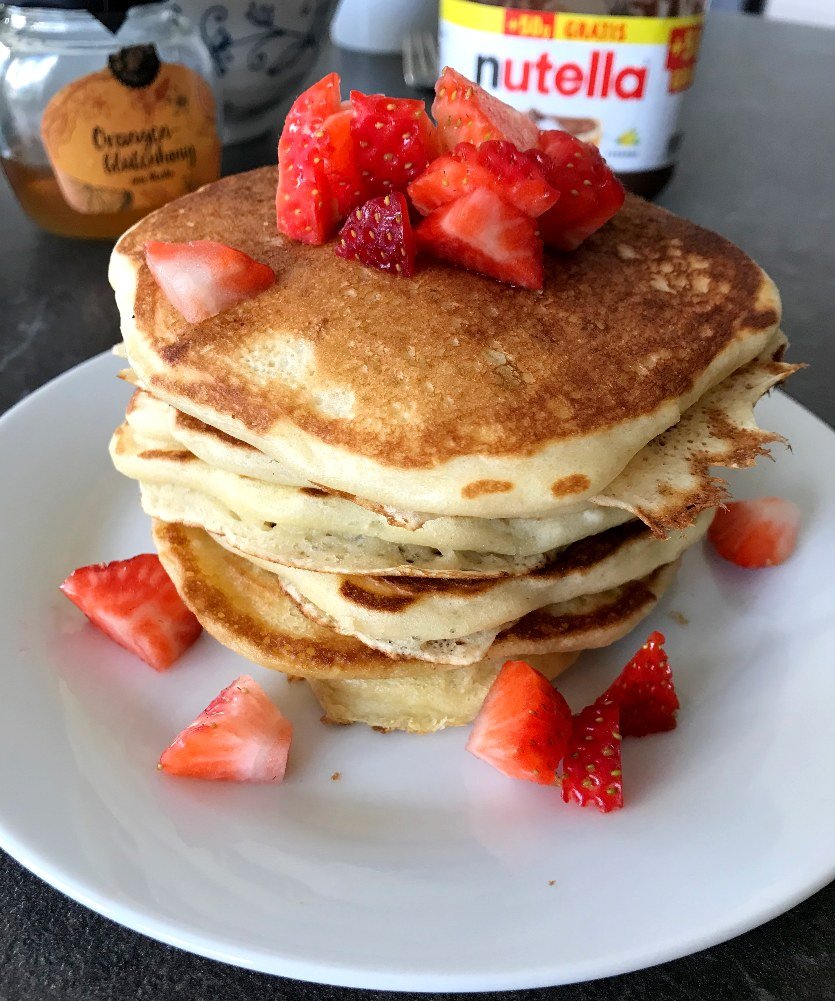 Stack of pancakes with honey and Nutella in background