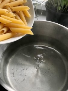 Penne pasta being added to boiling water.