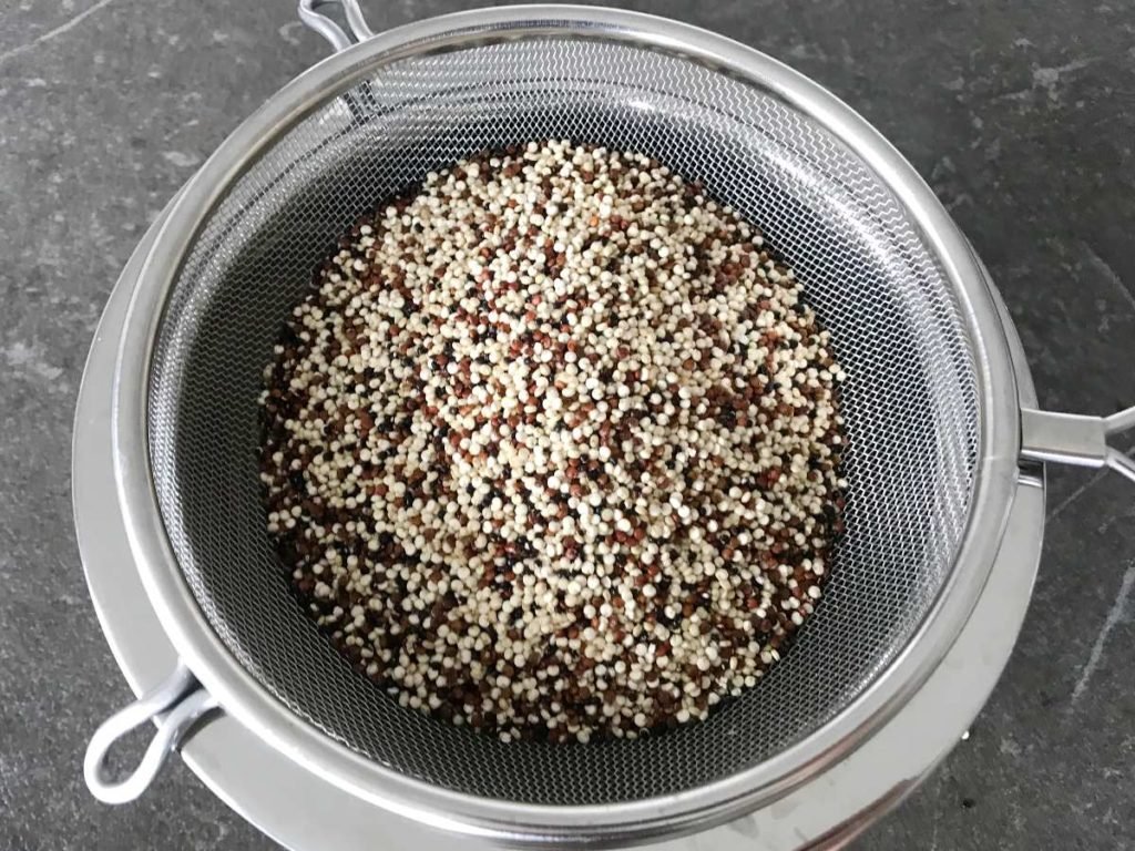 Quinoa in a sieve inside a stainless steel bowl