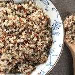 Cooked quinoa served in a bowl with a wooden spoon full of quinoa on the side.