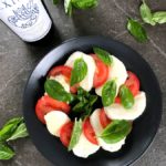 Tomato and Mozzarella slices with olive oil and herbed salt served on a plate.