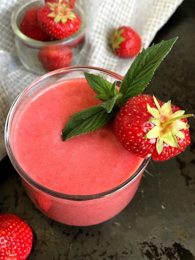 Strawberry smoothie in glass garnished with a strawberry and mint