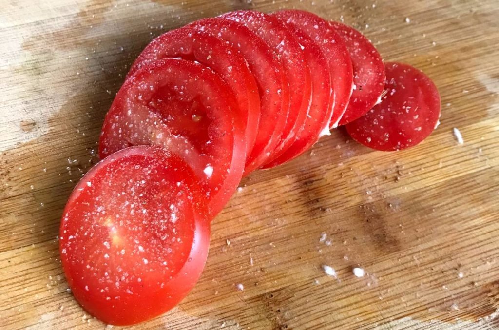 Tomato slices sprinkled with salt on a cutting board.