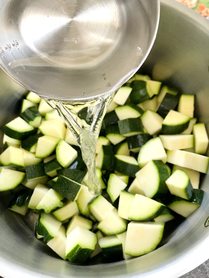 Water in measuring cup added to zucchini in pot