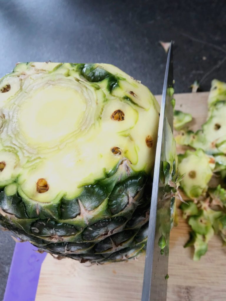 Pineapple rind being cut off with knife