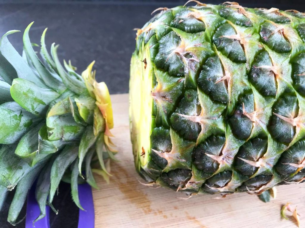 Pineapple on cutting board with top cut off.
