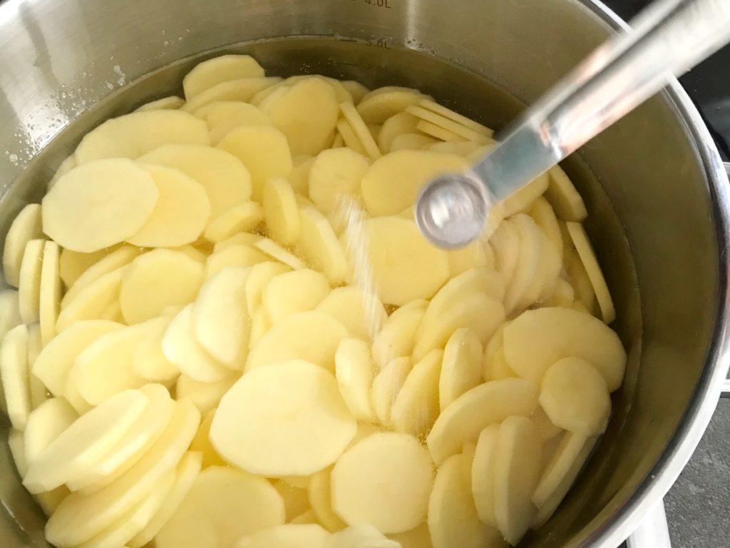 Potatoes in pot with water being salted