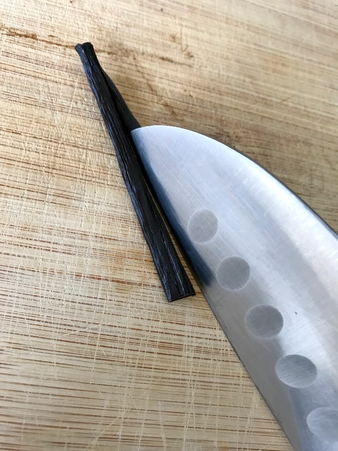 Vanilla bean cut in half and being cut in half lengthwise on a cutting board