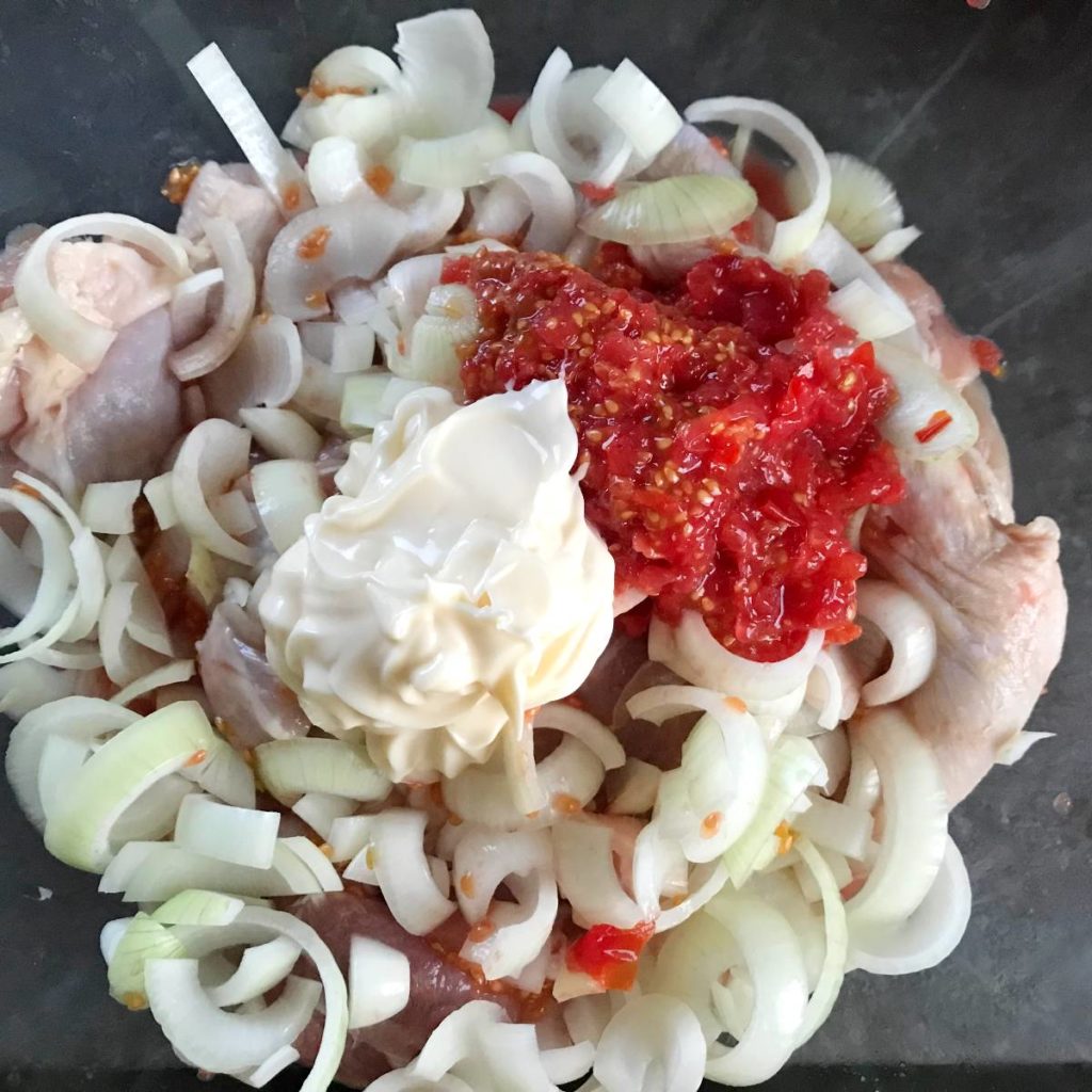 Chicken thighs with onions, mayo, and tomatoes marinade in a bowl