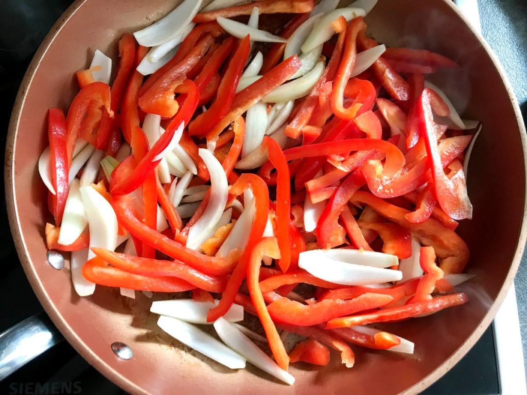 Red bell pepper and onions sautéed in skillet.