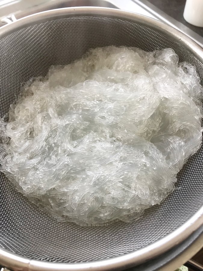 Cellophane noodles draining in a sieve.
