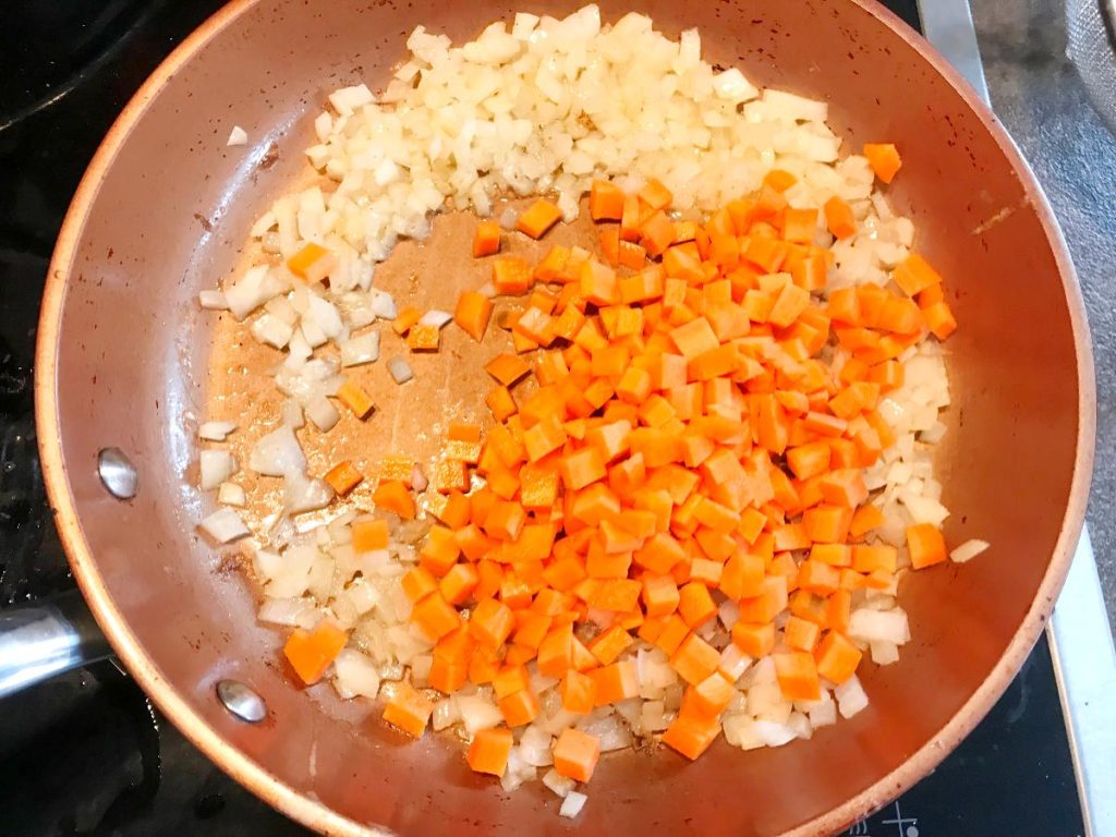 Carrots added to the onions sautéed in a skillet.
