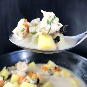 Chicken wild rice soup with mushrooms on a spoon against a black background