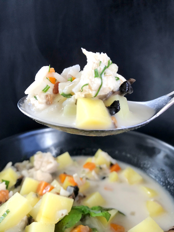 Chicken wild rice soup with mushrooms on a spoon against a black background