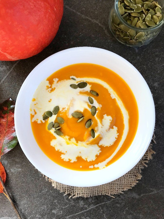 Creamy red kuri squash soup served in a bowl with cream.