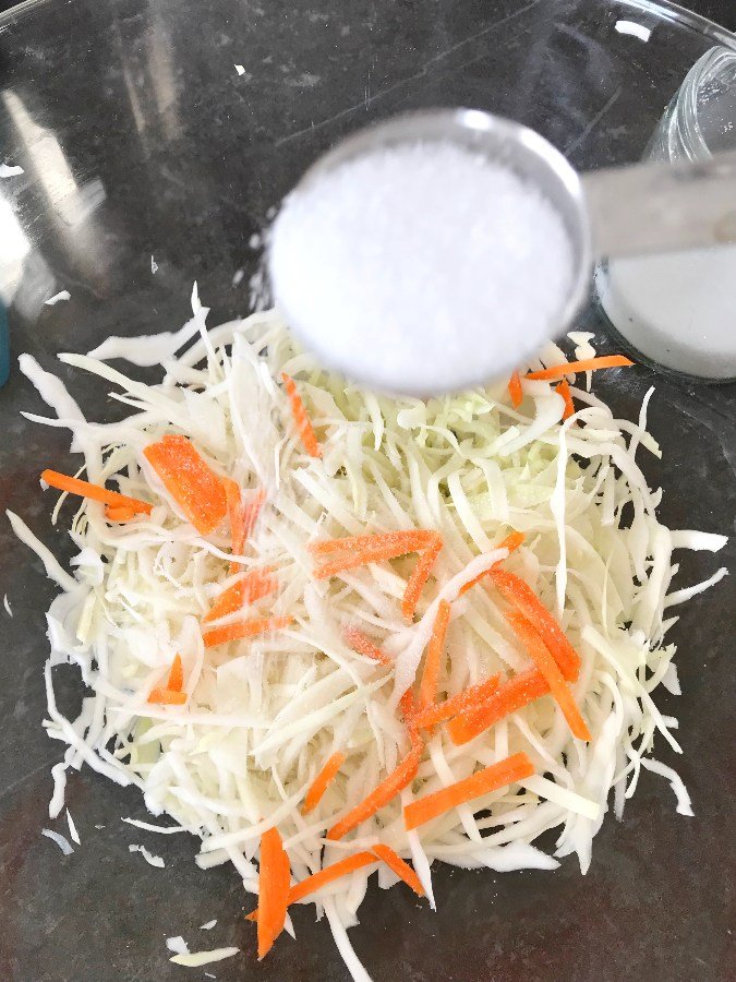 Salt sprinkled on layer of shredded cabbage and carrots.