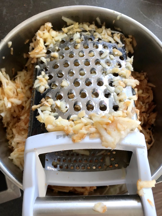 Box grater and grated apples in a big pot.