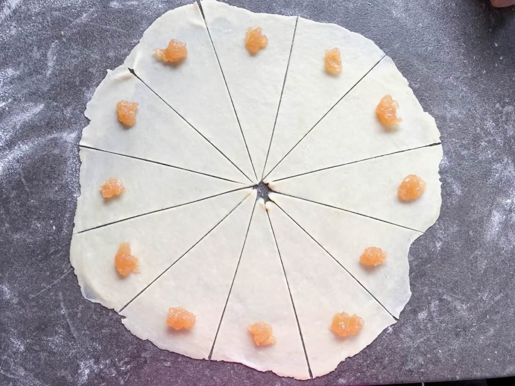 Rugelach dough rolled out and cut with apple jam placed on each piece.