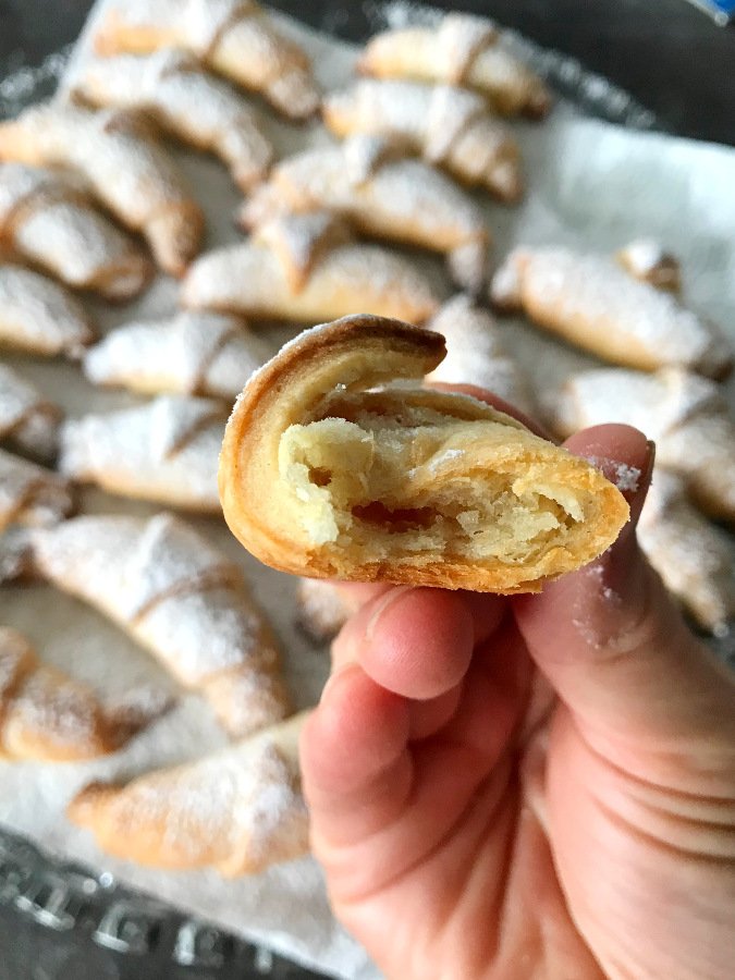 A hand holding an apple rugelach cookie with the rest of cookies in the background.