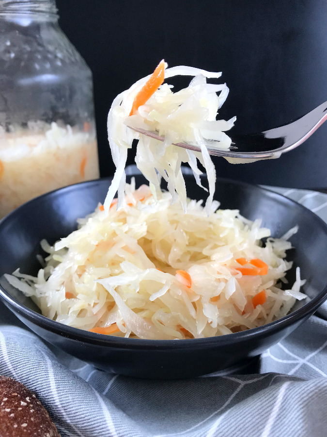 Homemade Sauerkraut lifted on a fork from  a black salad bowl.