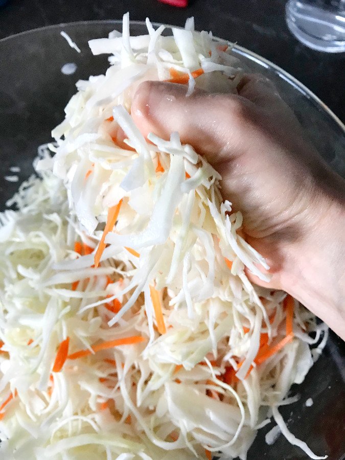 Squeezing and massaging shredded cabbage to release juices.