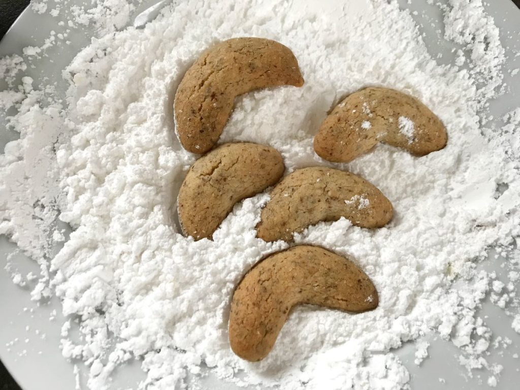 Hot Vanilla Kipferl cookies placed into powdered sugar mixture.