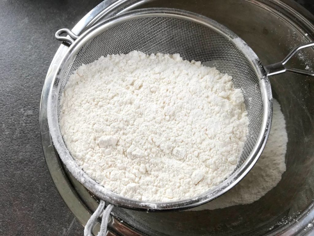 Flour sifted into a bowl using a sieve.