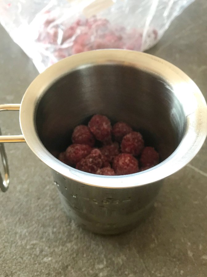 Frozen raspberries placed in a stainless steel pitcher or cup.