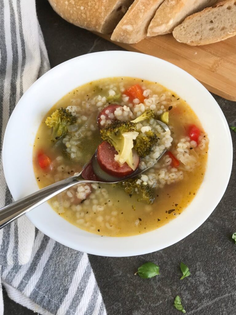 Sausage stew with broccoli and barley served in a bowl with sourdough bread on the side.