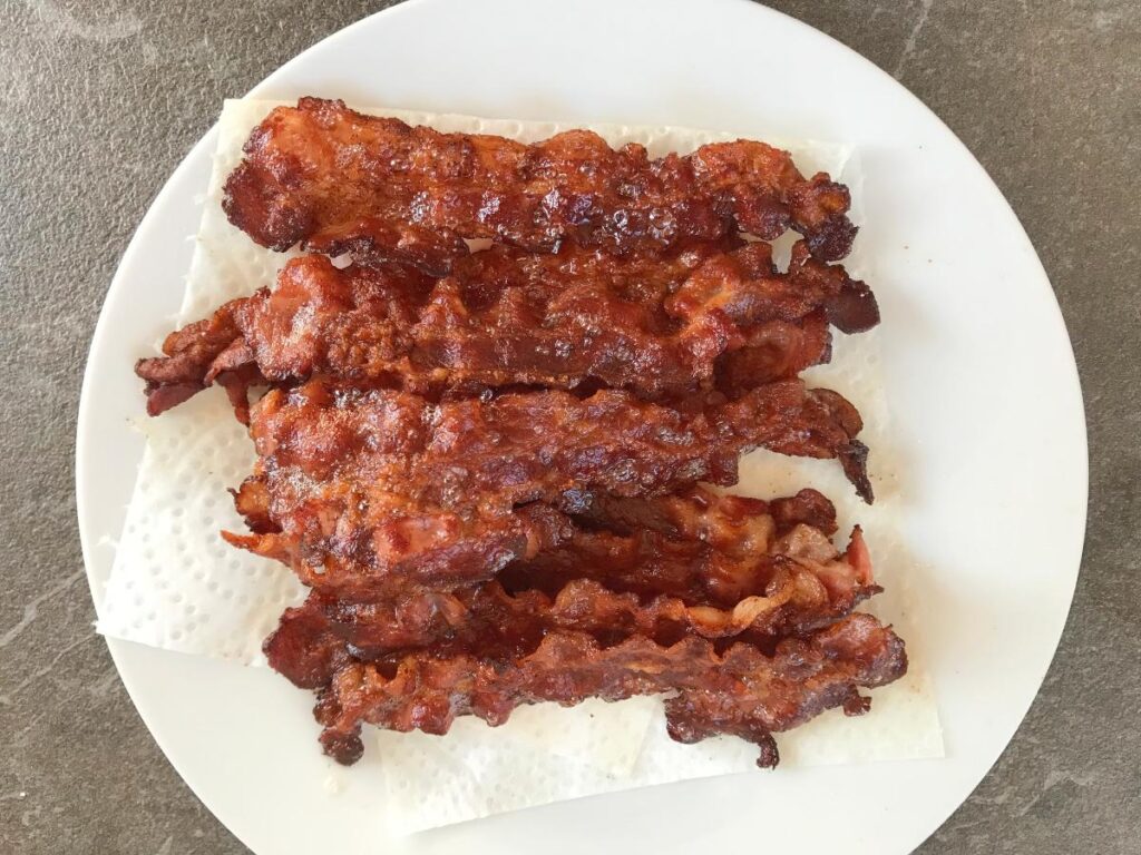 Fried bacon strips on a napkin on a plate.