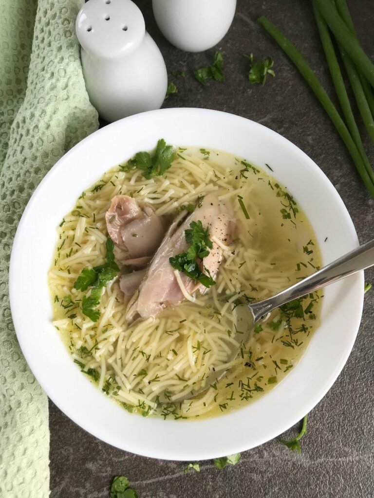 Egg noodle soup with chicken served in a bowl with chicken meat and greens.