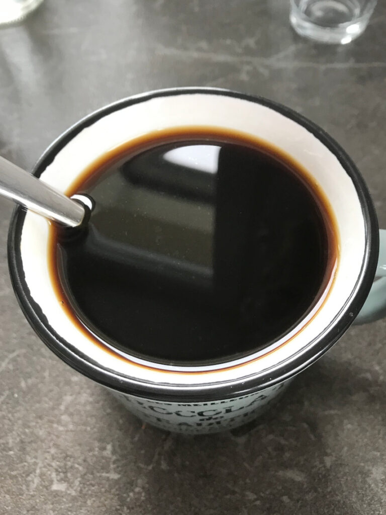 Strong black coffee in a mug with a spoon.