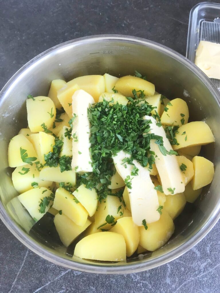 Butter, parsley and salt added to boiled potatoes in a pot.