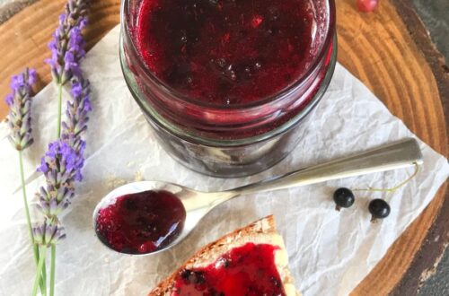 Black currant jam in a jar, on a spoon and spread on bread with butter.