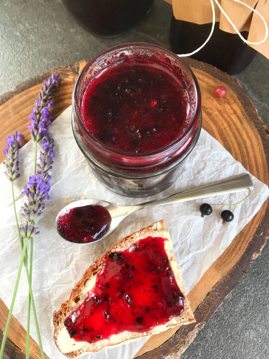 Black currant jam in a jar, on a spoon and spread on bread with butter.