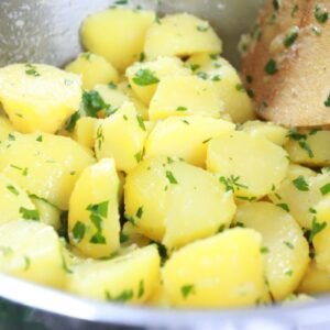 Butter potatoes with parsley in a pot with a wooden spoon.