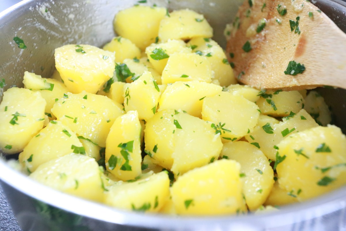 Butter potatoes with parsley in a pot with a wooden spoon.