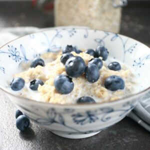 Oatmeal porridge served in a bowl with milk and blueberries.