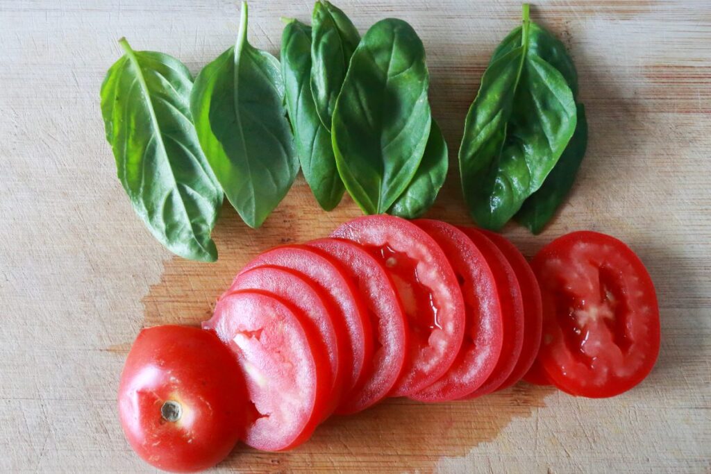 Sliced tomatoes and basil leaves on a bamboo cutting board