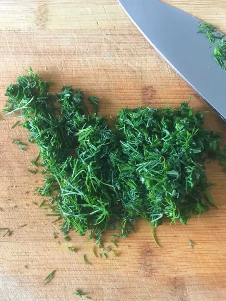 Chopped dill and parsley on a cutting board.
