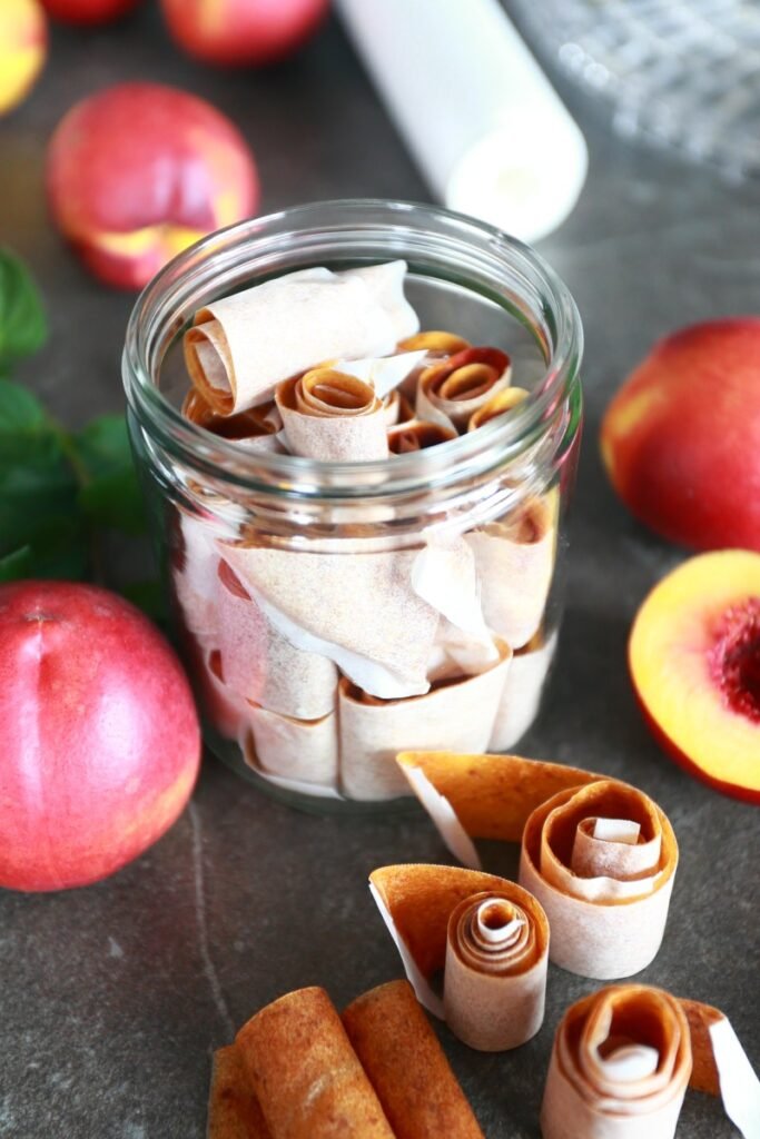 Homemade Fruit Roll Ups in a glass surrounded by nectarines and additional fruit roll ups.