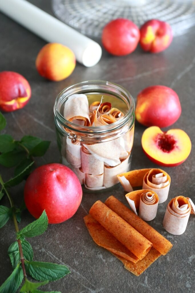 Homemade Fruit Roll Ups in a glass surrounded by nectarines.