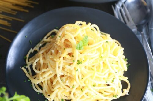 Fried spaghetti on a black plate surrounded by uncooked spaghetti, kitchen towel and basil.