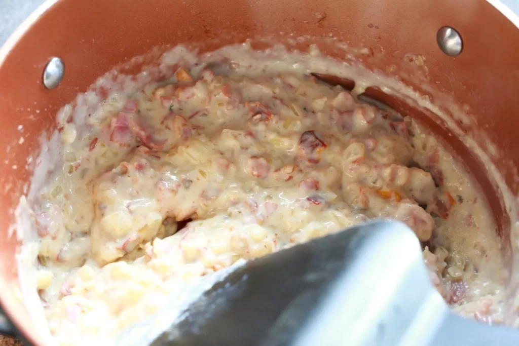 Creamy sauce with bacon onion and tomatoes being stirred in a pot