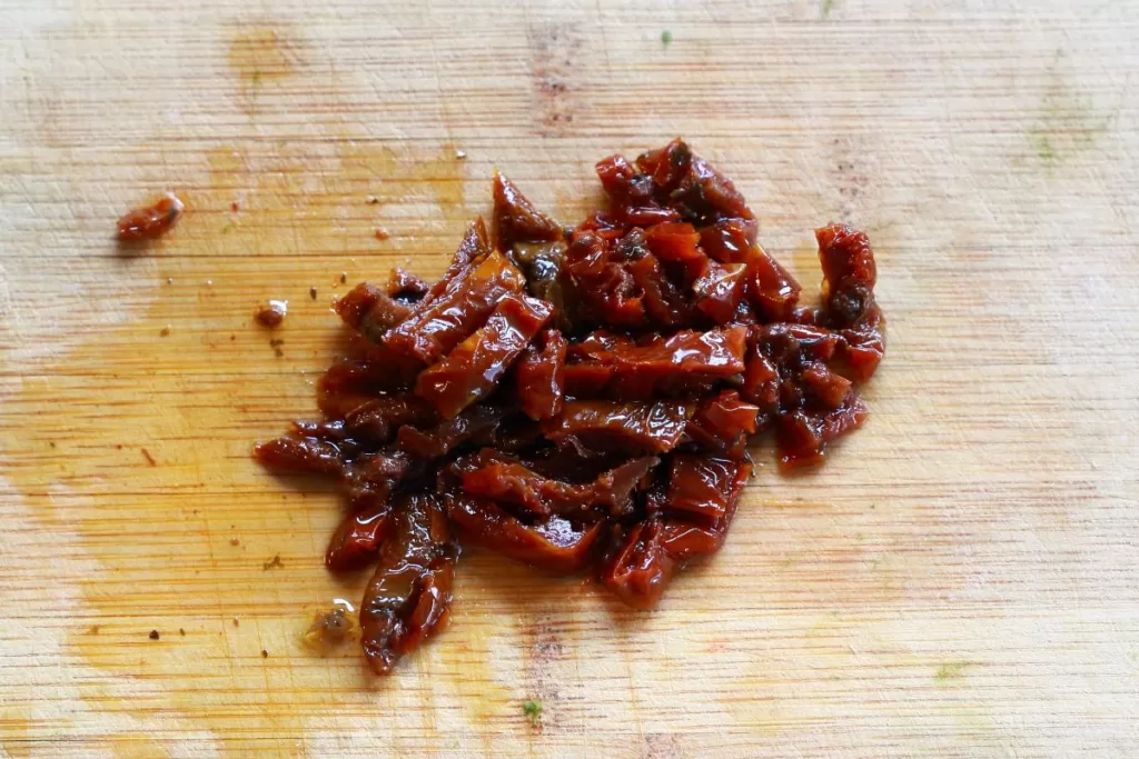Diced sun dried tomatoes in oil on a cutting board.