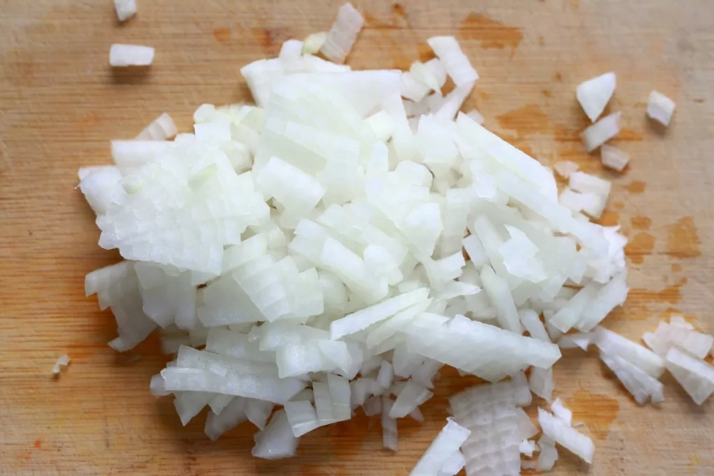 Minced white onion on a bamboo cutting board.