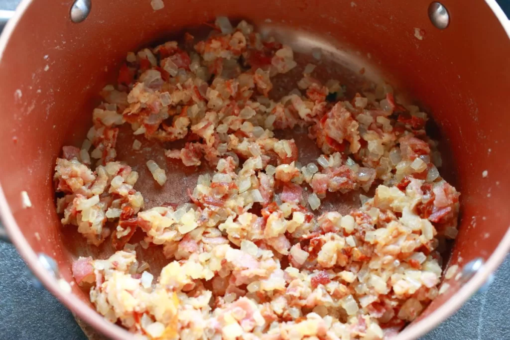 Fried bacon pieces with onion tomatoes and flour in a small pot.