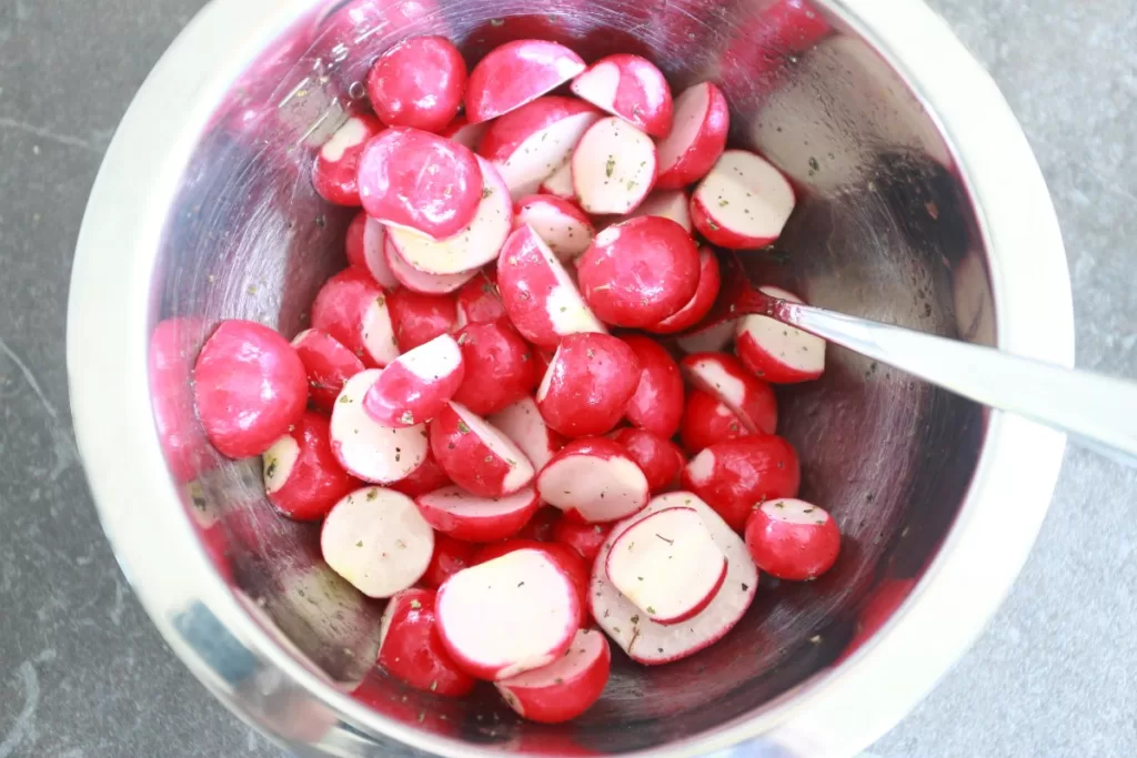 Radish halves in a bowl mixed with oil and seasonings